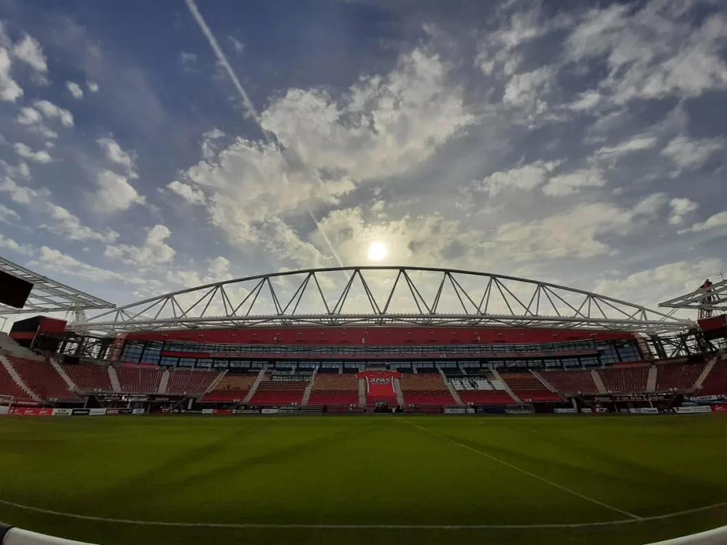 Wide-angle view of an empty soccer stadium under a partly cloudy sky.