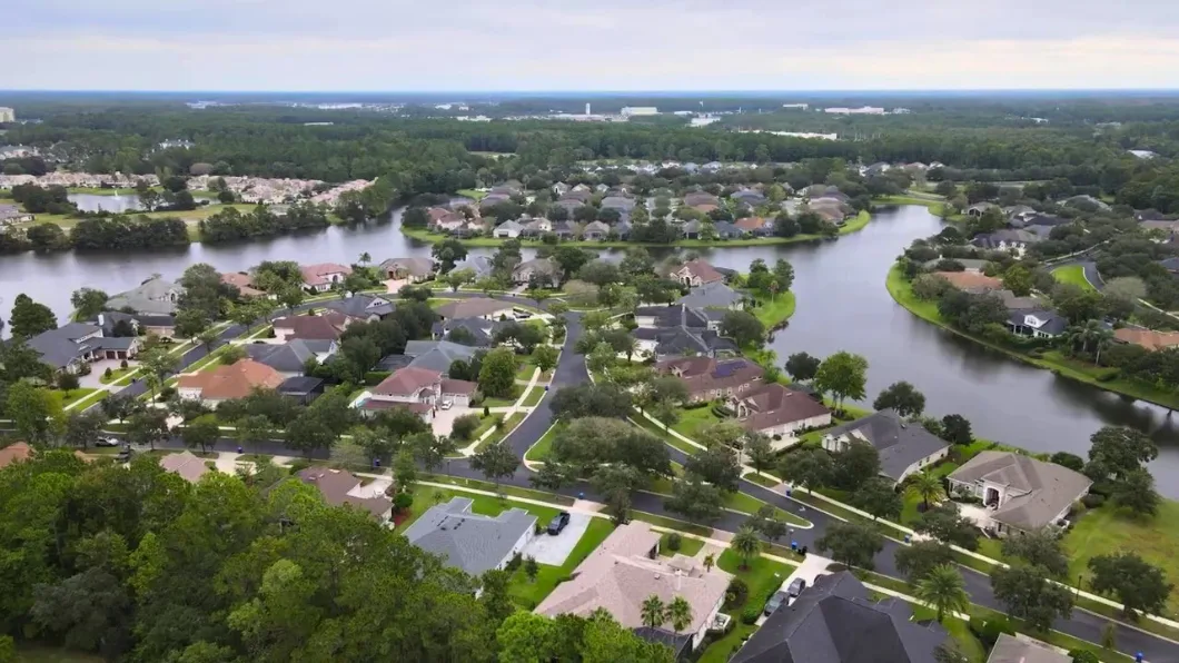 An aerial view of a suburban neighborhood in St. Johns County, Florida, with homes along winding streets and a calm river under an overcast sky.