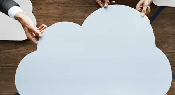 Four hands hold up a large, light blue cloud shape against a wooden background.