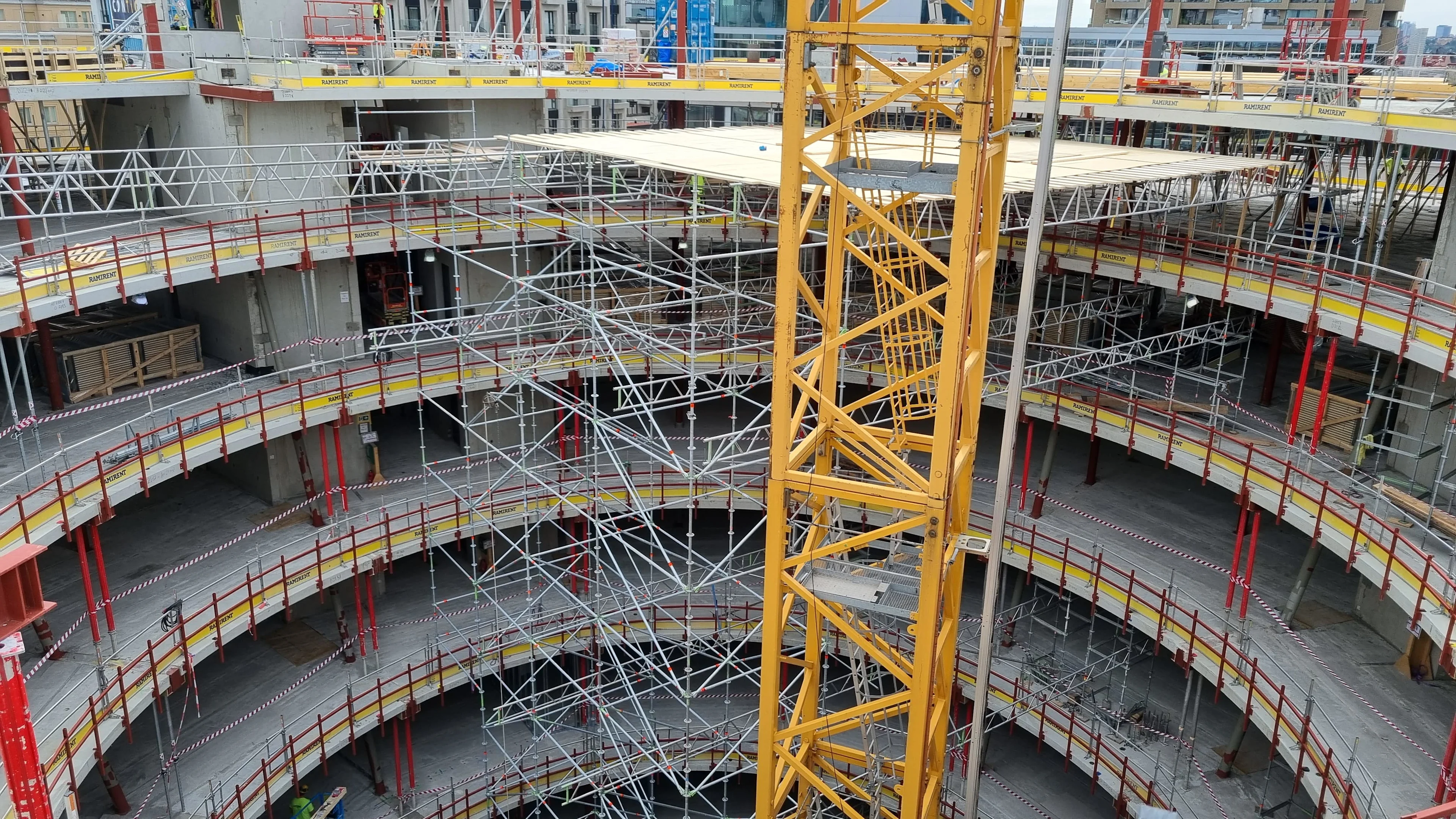 A crane arm is visible against scaffolding and concrete structures of a large, multi-story building under construction.