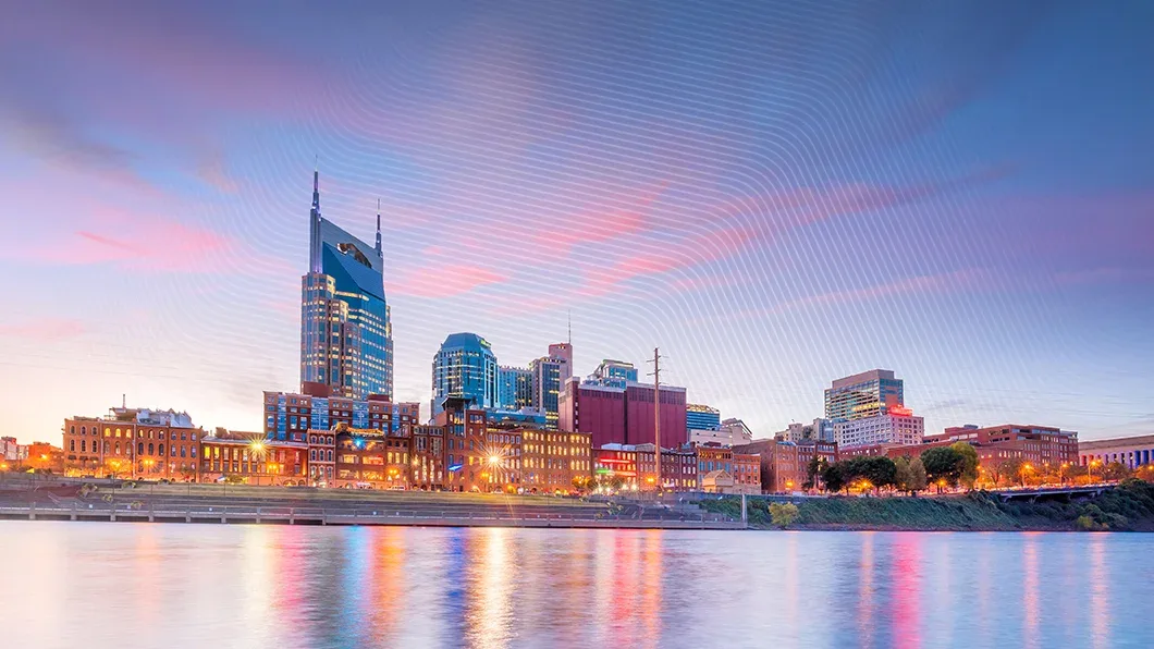 Nashville skyline at dusk: AT&T 'Batman Building' skyscraper and commercial structures reflect on Cumberland River, symbolizing urban development.