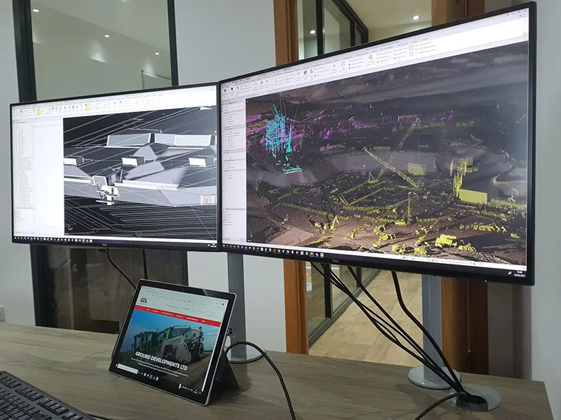 Dual monitors display 3D modeling and point cloud data of construction projects.