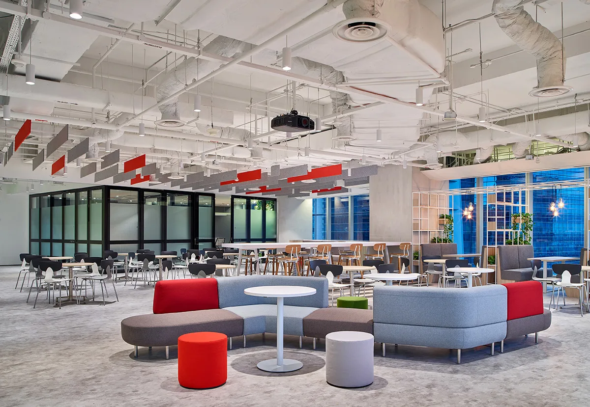 Modern office lounge area with modular seating, tables, and a glass-walled meeting room.