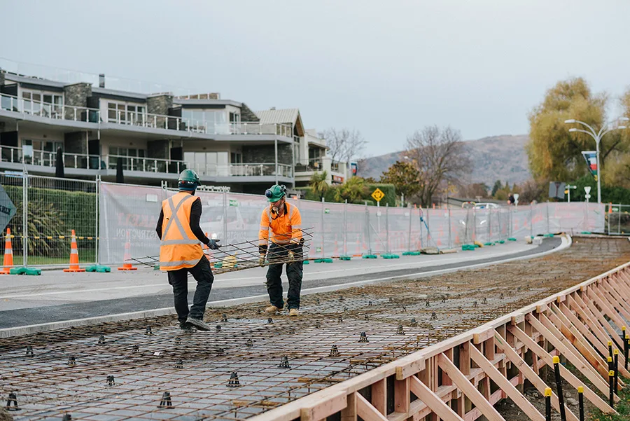 Construction workers carry rebar for concrete pouring at a job site.