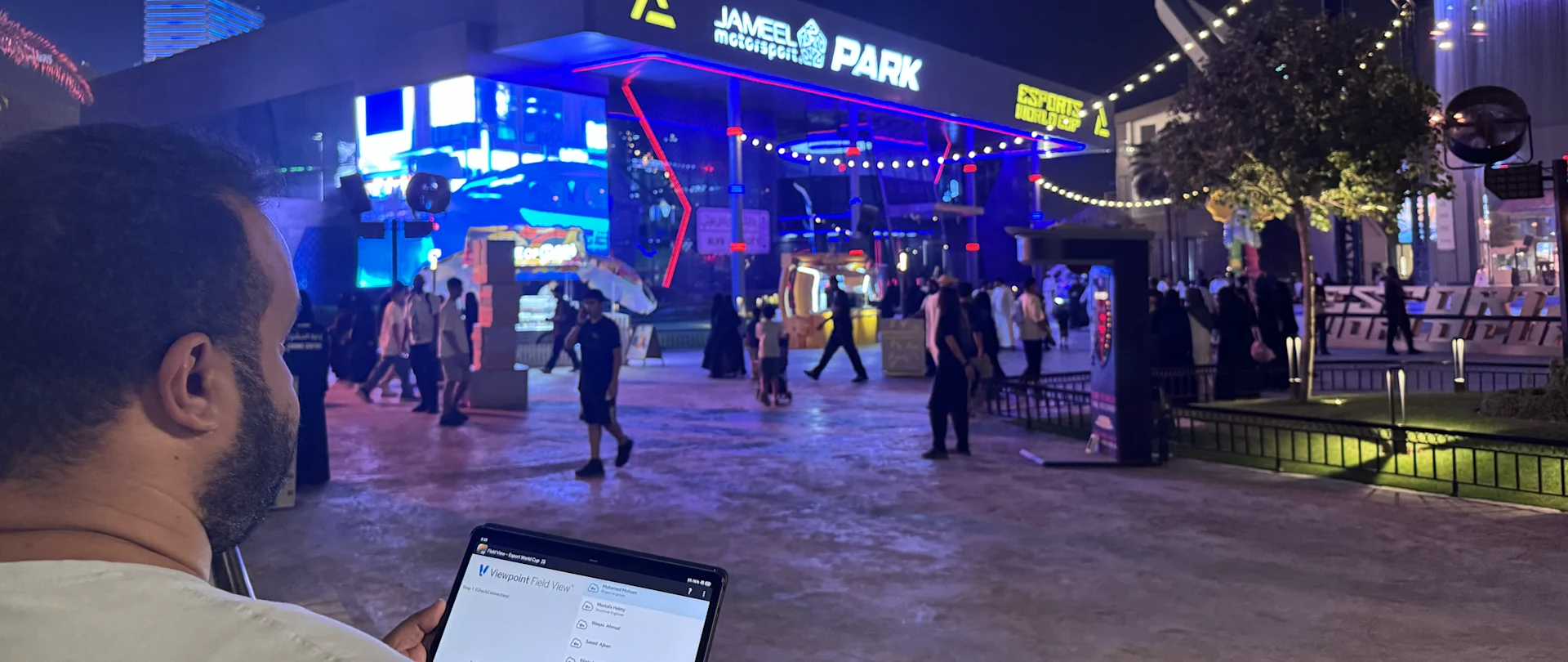 A man holds a tablet in front of the Jameel Motorsport Park building at the Esports World Cup.