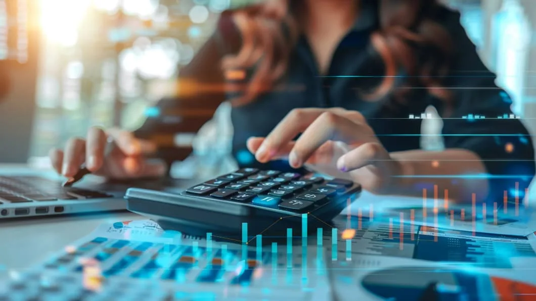 Close-up of hands using a calculator and laptop with digital overlays of financial growth charts.
