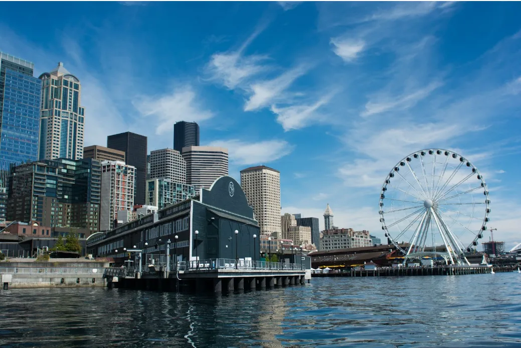 Seattle skyline with the Great Wheel and waterfront buildings under a blue sky.