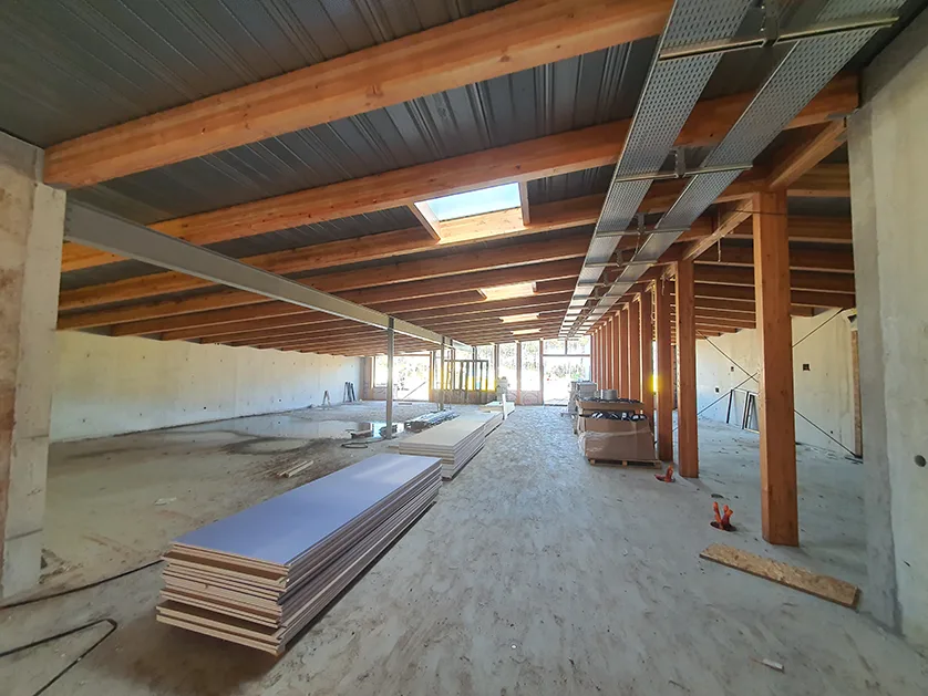 Interior view of a building under construction, with exposed wooden beams, concrete walls, and stacked building materials.