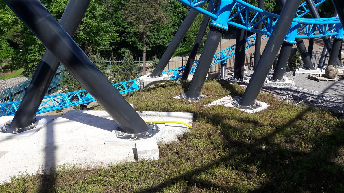 A view from above of the construction of a roller coaster with large black supports and bright blue tracks.
