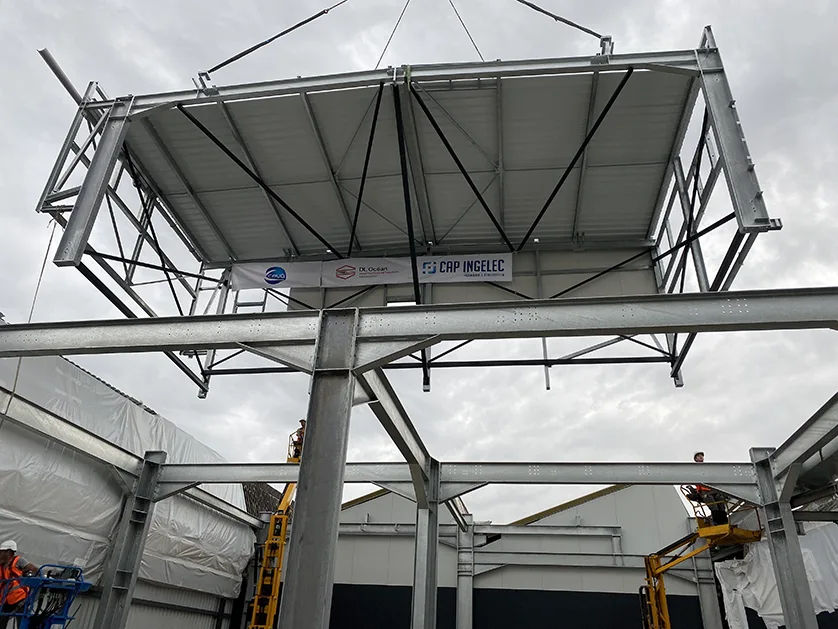 A large section of a steel building is being lifted by a crane.