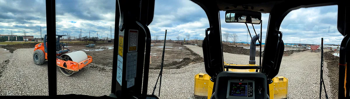 View from inside a construction vehicle, showing a roller compactor and a construction site.