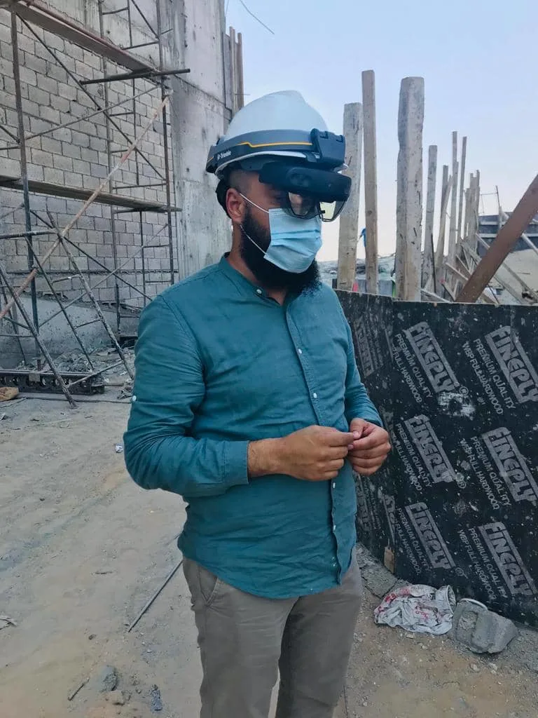 Man wearing hard hat, AR glasses, and mask at a construction site with scaffolding.