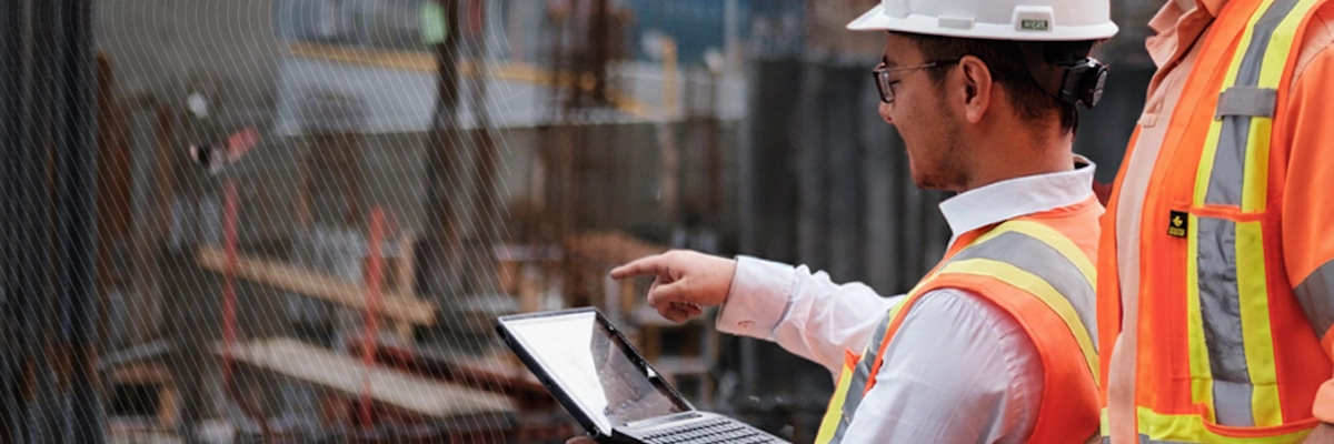 Construction workers in safety gear using a laptop at a building site