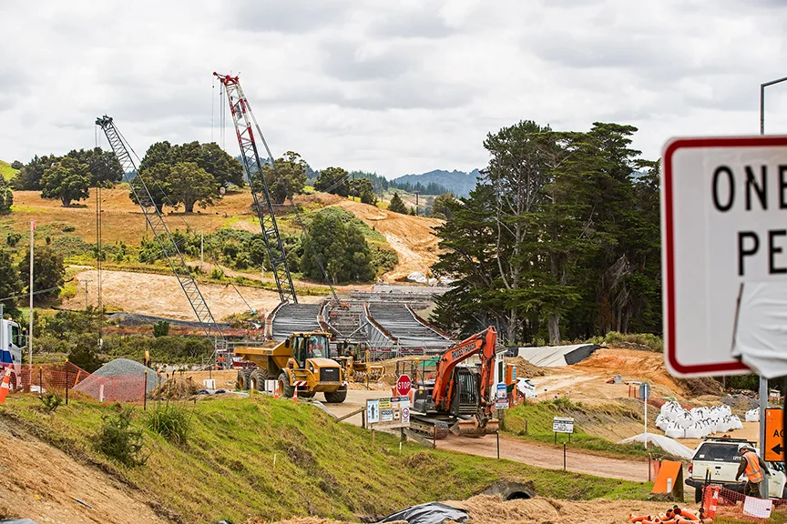 Construction site with cranes, excavators, dump truck, and ongoing bridge building.