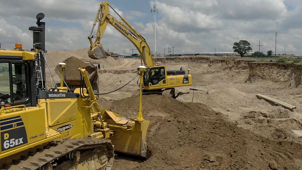 Yellow Komatsu bulldozer and excavator with Trimble GPS technology moving earth on a large construction site.