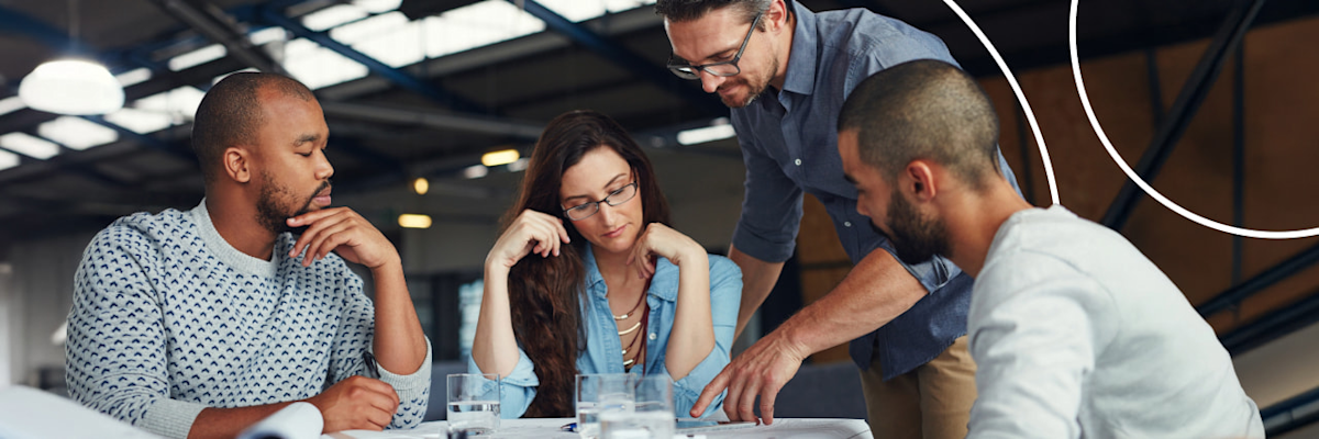 Diverse team of colleagues leaning over a table in a modern office, focused on a collaborative project.