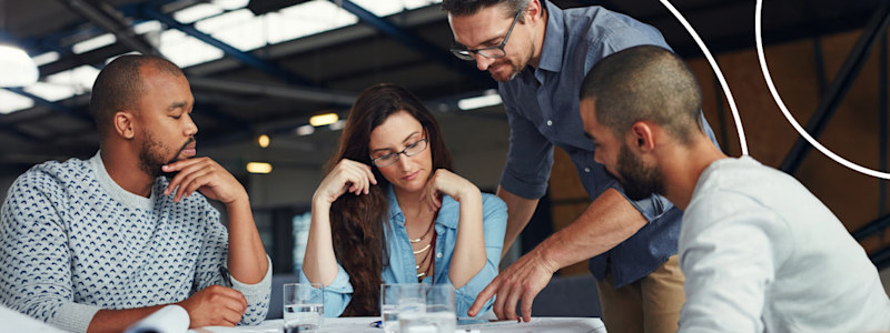 Diverse team of colleagues leaning over a table in a modern office, focused on a collaborative project.
