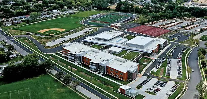Aerial view of a modern school complex featuring athletic fields and a large parking lot.