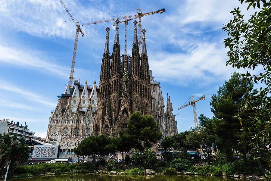 Sagrada Familia under construction, with cranes visible against a blue sky.