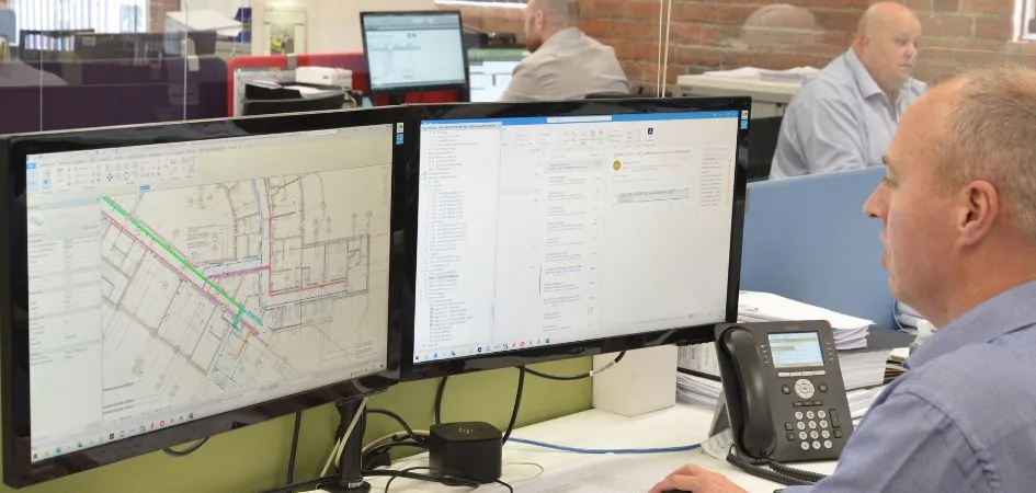 Engineer reviews MEP design on dual monitors displaying floor plans and project data.