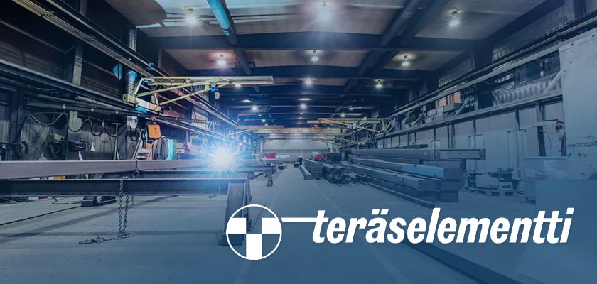 A welder works on a steel beam in a large factory, with stacks of metal beams in the background.