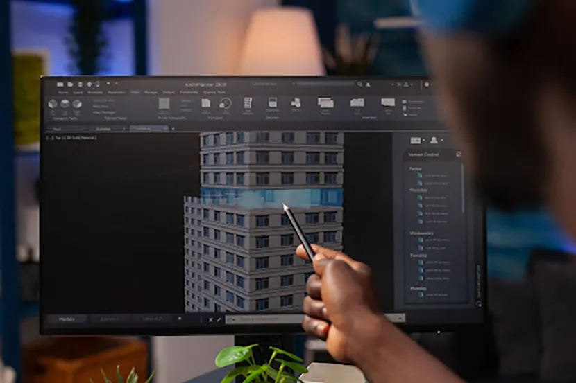 A person's hand is shown using a stylus to interact with a 3D model of a building on a computer screen.