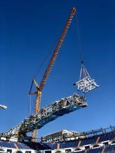 A crane lifts a large metal structure over the Santiago Bernabéu Stadium.