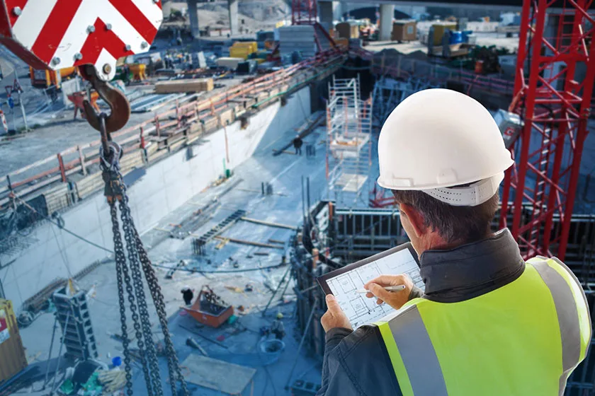 Mann auf Baustelle greift über ein Tablet auf Informationen des Bauprojekts zu.