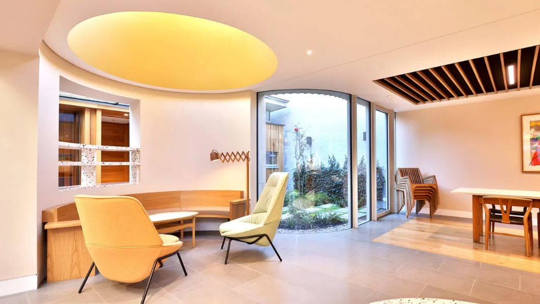 Cozy modern lounge with curved windows, yellow ceiling light, and stylish mid-century armchairs.