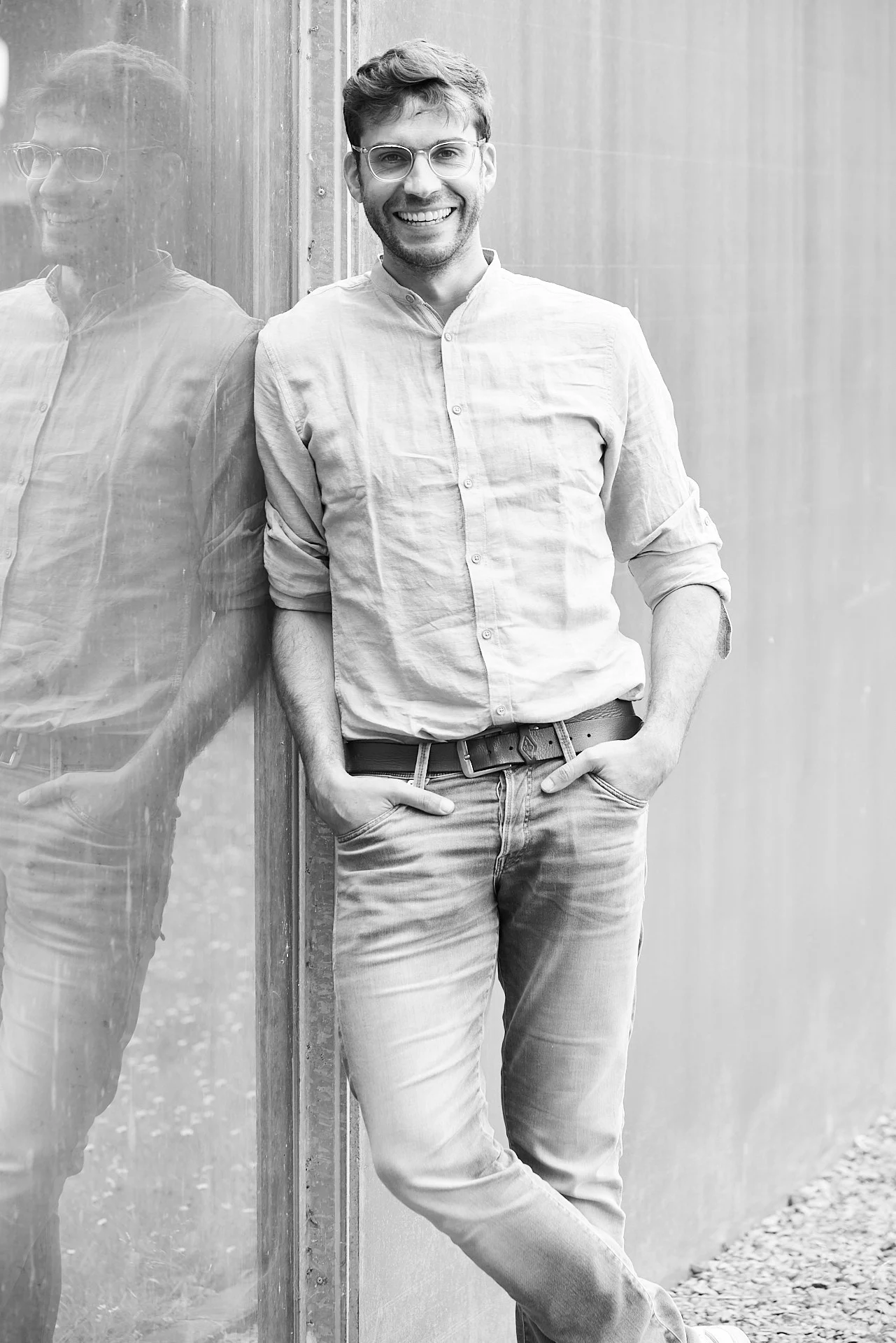 Black and white portrait of Simon Scharlaken, leaning against a wall with his reflection visible.