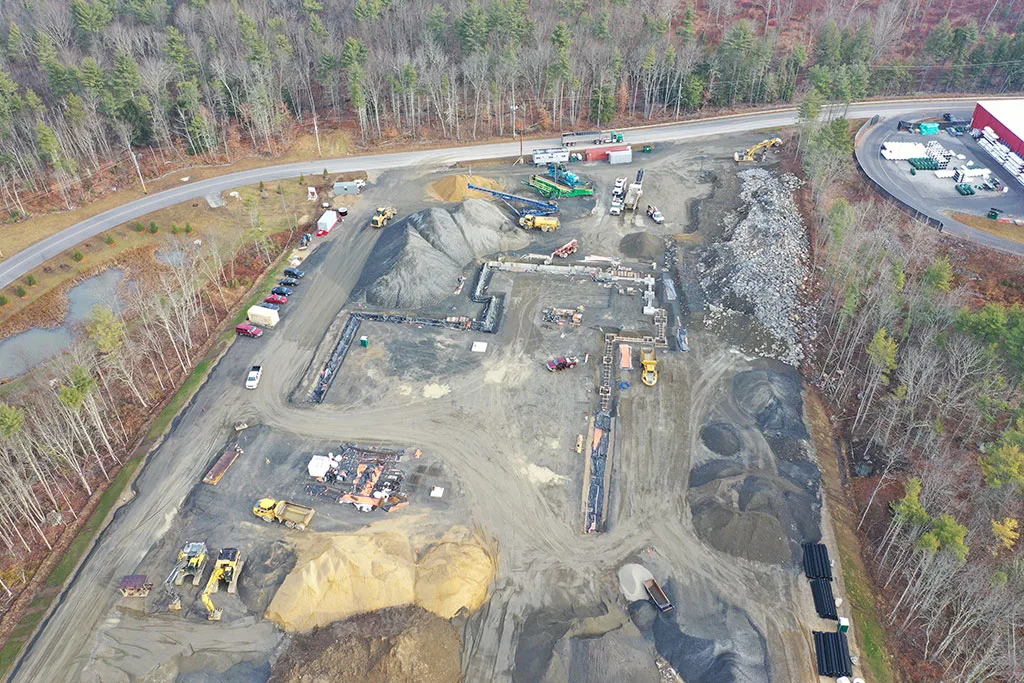 Construction site with heavy machinery, piles of gravel, and building foundations.