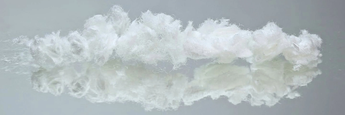 A cluster of soft, white wood pulp fibers resting on a reflective glass surface.