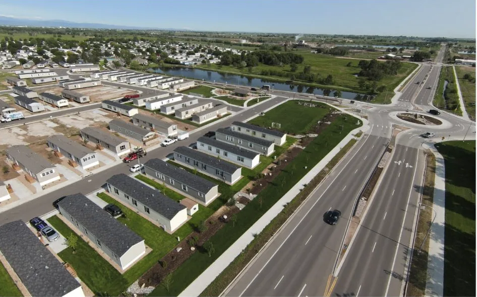 Aerial view of a residential development with rows of manufactured homes adjacent to a newly constructed road intersection.
