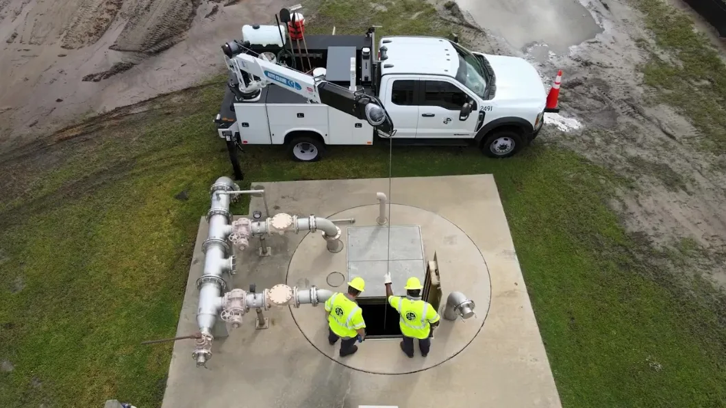 Two utility workers wearing hardhats and safety vests inspect wastewater treatment infrastructure after a rainstorm in St. Johns County, Florida.