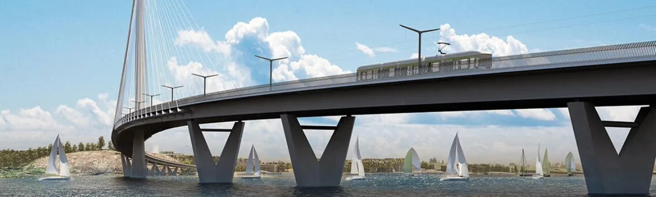 A modern bridge with a light rail train crosses a body of water, featuring sailboats and a natural, tree-covered shoreline.