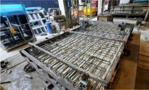 A large, flat piece of rebar laid out in a grid pattern within a mold in a factory setting.