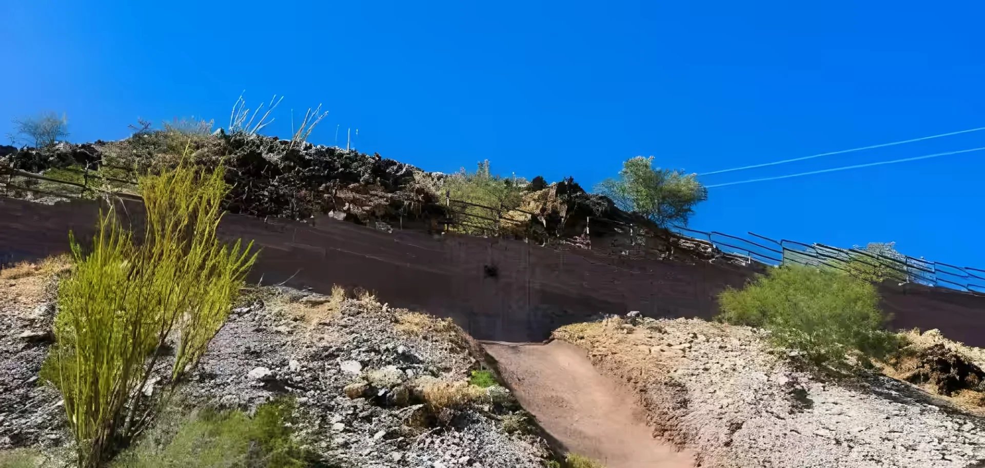 View from the base of a steep, rocky slope on North Mountain, showing a dirt trail leading up to a reinforced retaining wall.
