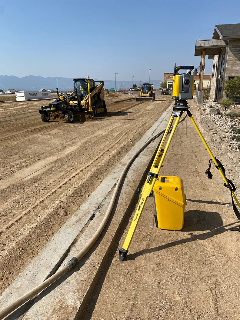 Construction site with heavy machinery and surveying equipment on a sunny day.