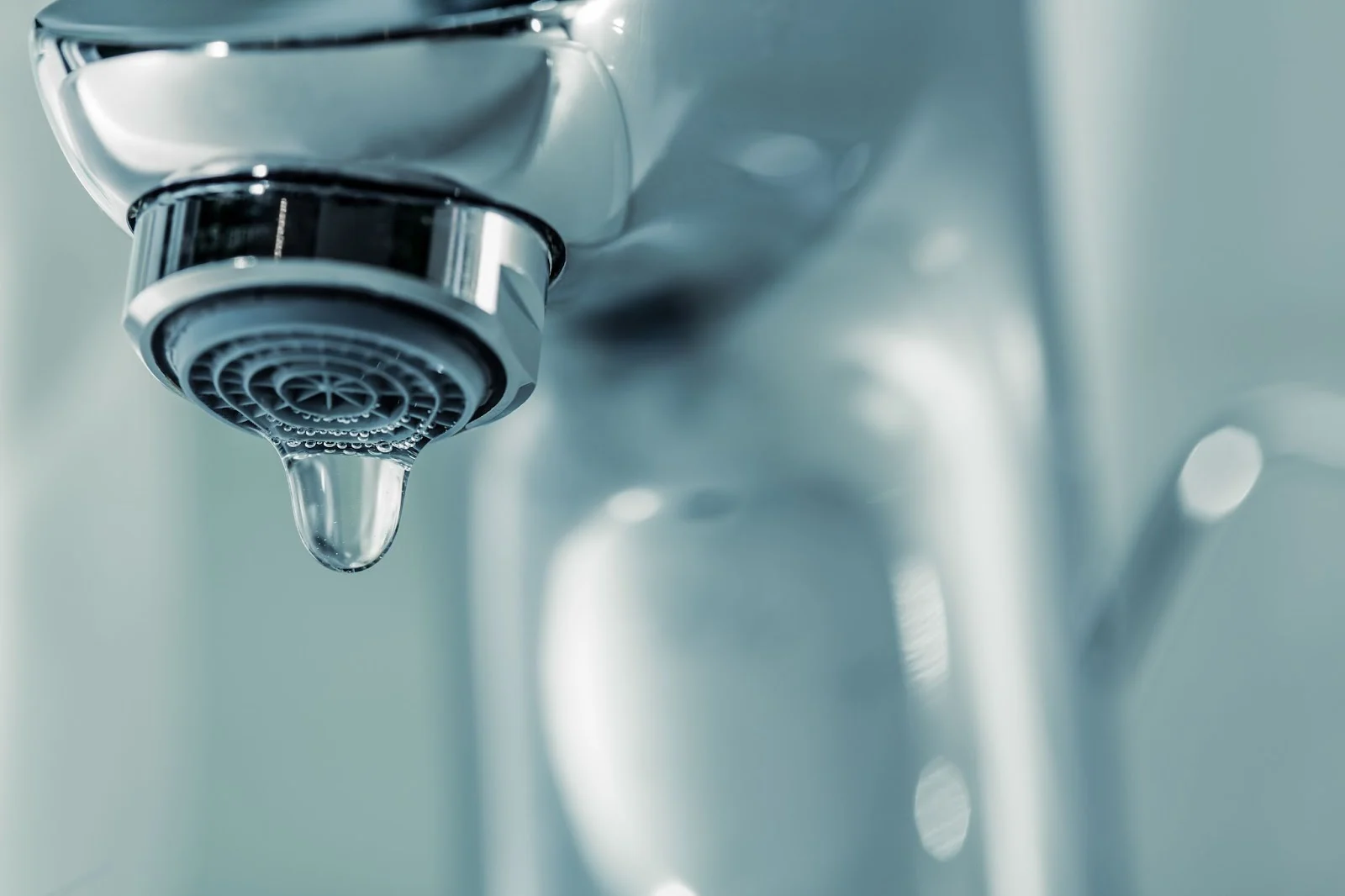 Close-up of a water droplet falling from a chrome faucet, symbolizing hygiene and purity.