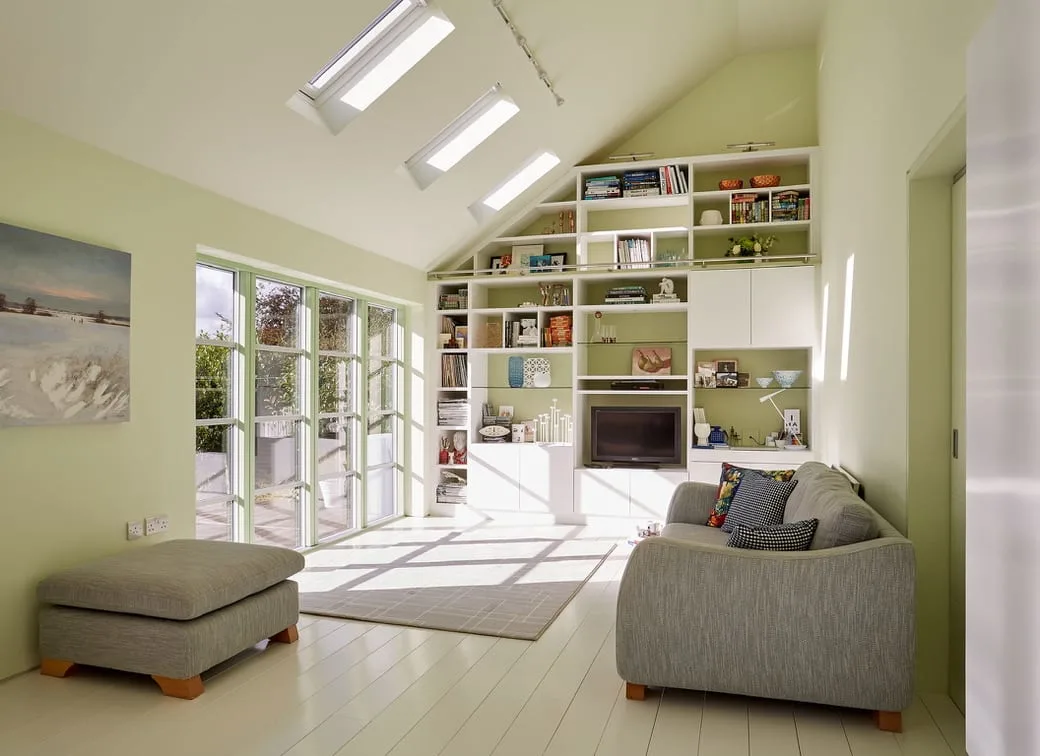 a custom-designed living room/study with a wall of windows, light green walls, and white built-in shelving