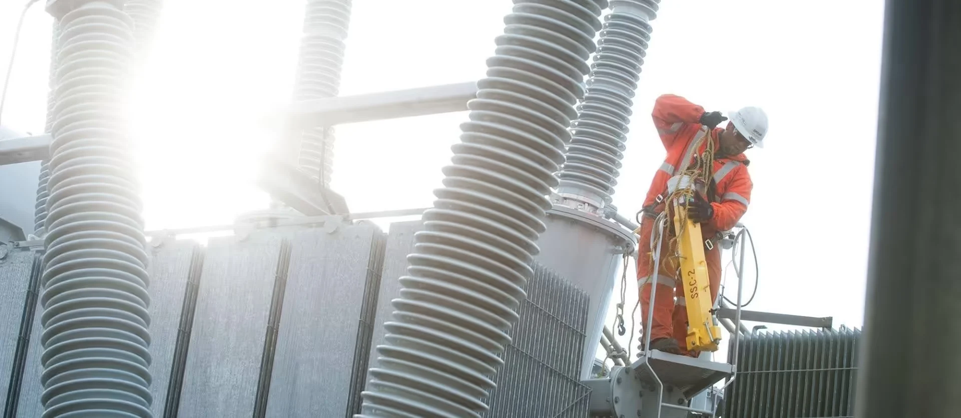 An EPCOR utility worker in high-visibility gear performing maintenance on high-voltage substation insulators.