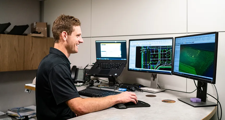 Man smiling while working on CAD software on a multi-monitor setup.