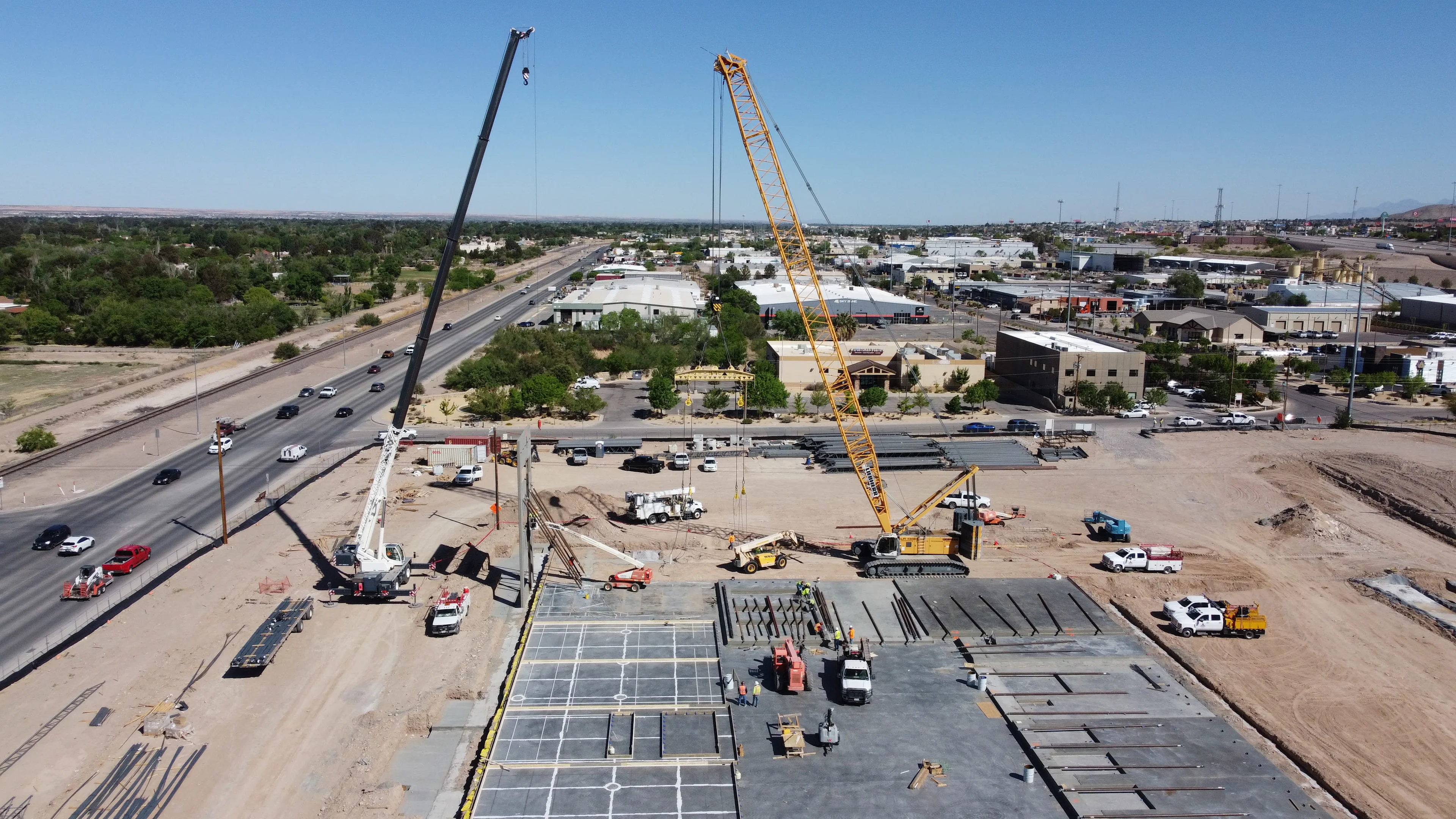 Construction site with two large cranes and precast concrete panels on a sunny day.