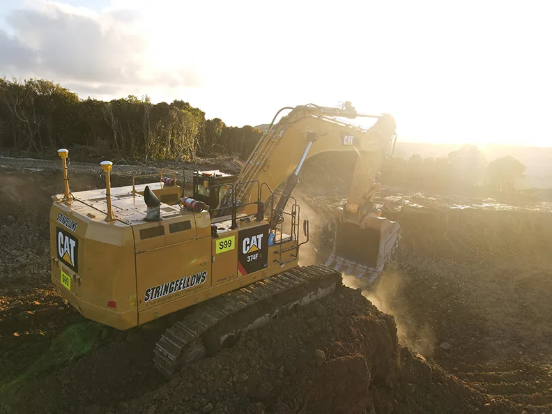 Yellow CAT excavator digging a large amount of dirt with dust and debris flying in the air.