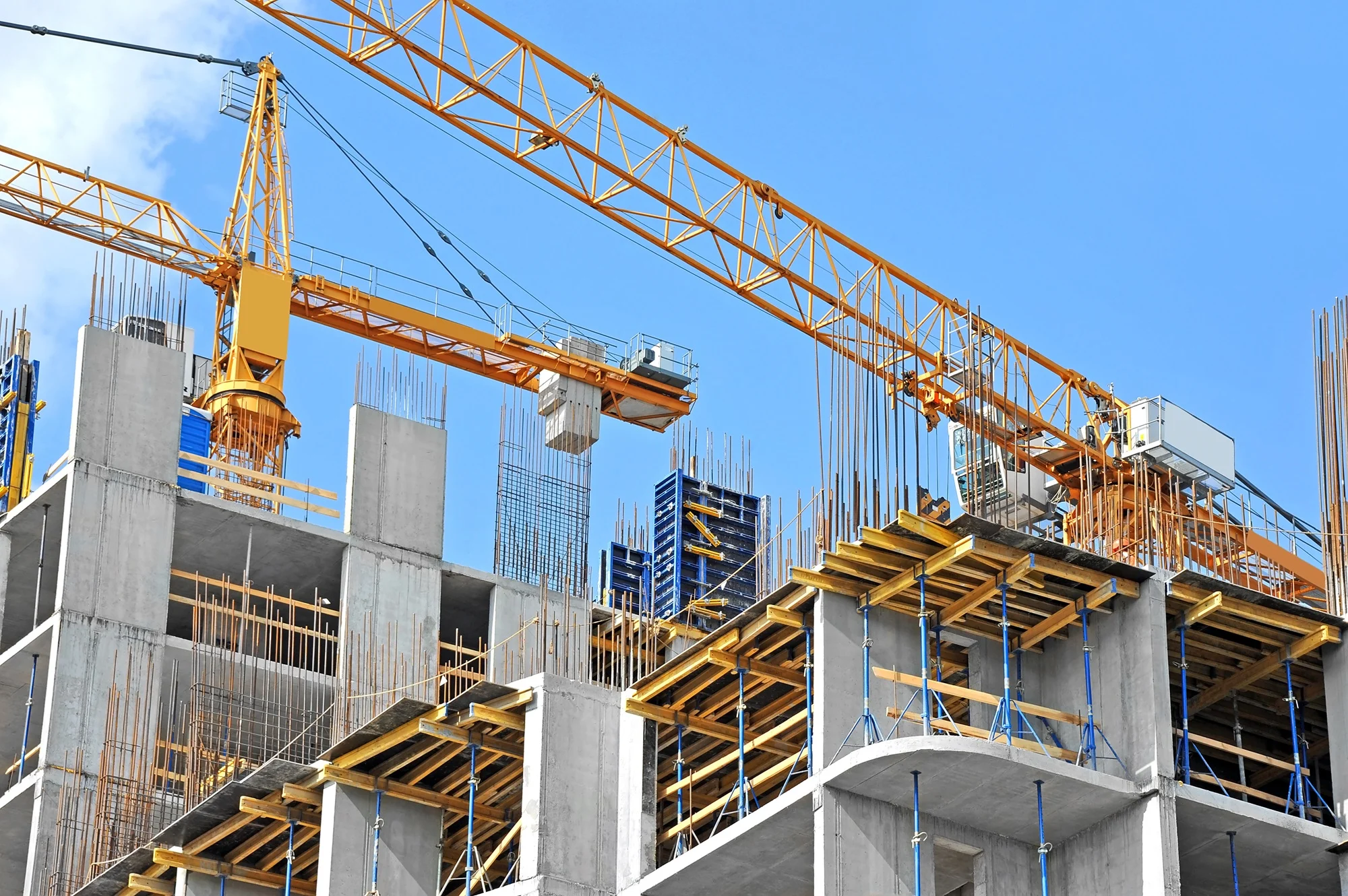 Construction crane over a building under construction with concrete framework against a blue sky.