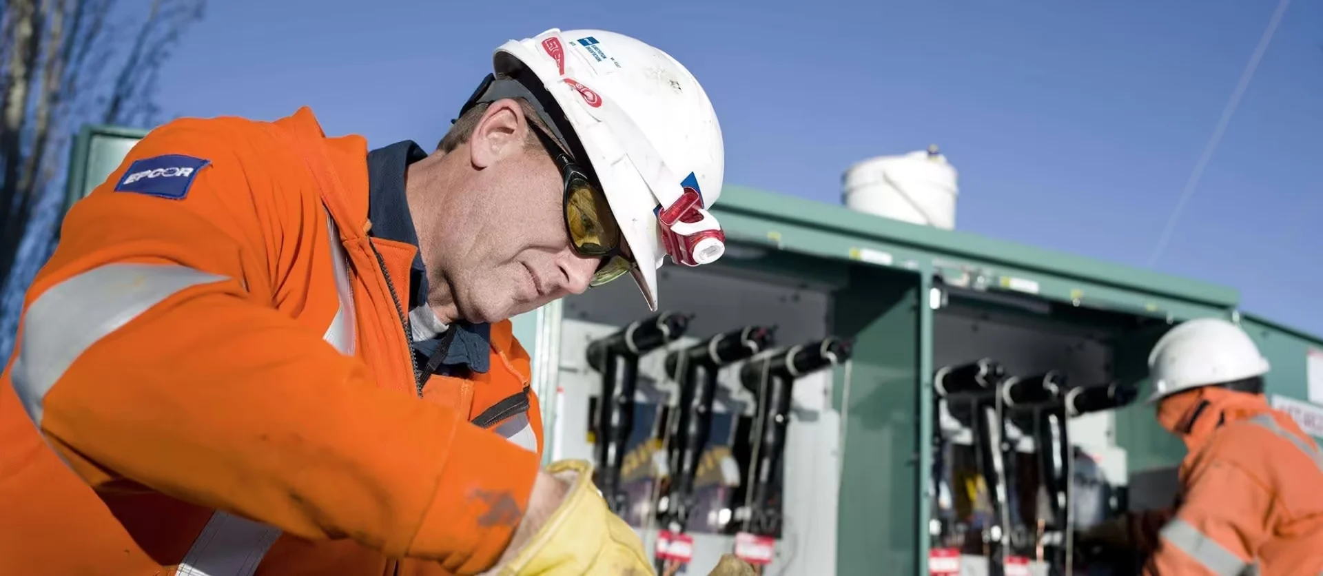 Close-up of an EPCOR technician in a hard hat and safety glasses inspecting electrical transformer components.