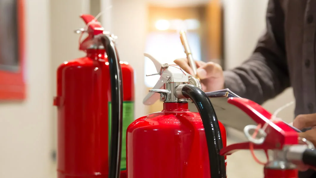 A close-up of a technician inspecting red fire extinguishers and writing notes on a clipboard.