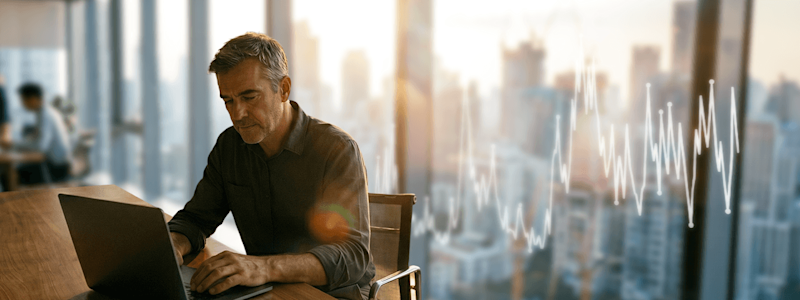 Man works on laptop, financial growth chart overlaid on bright city skyline. Suitable for AECO data analysis.