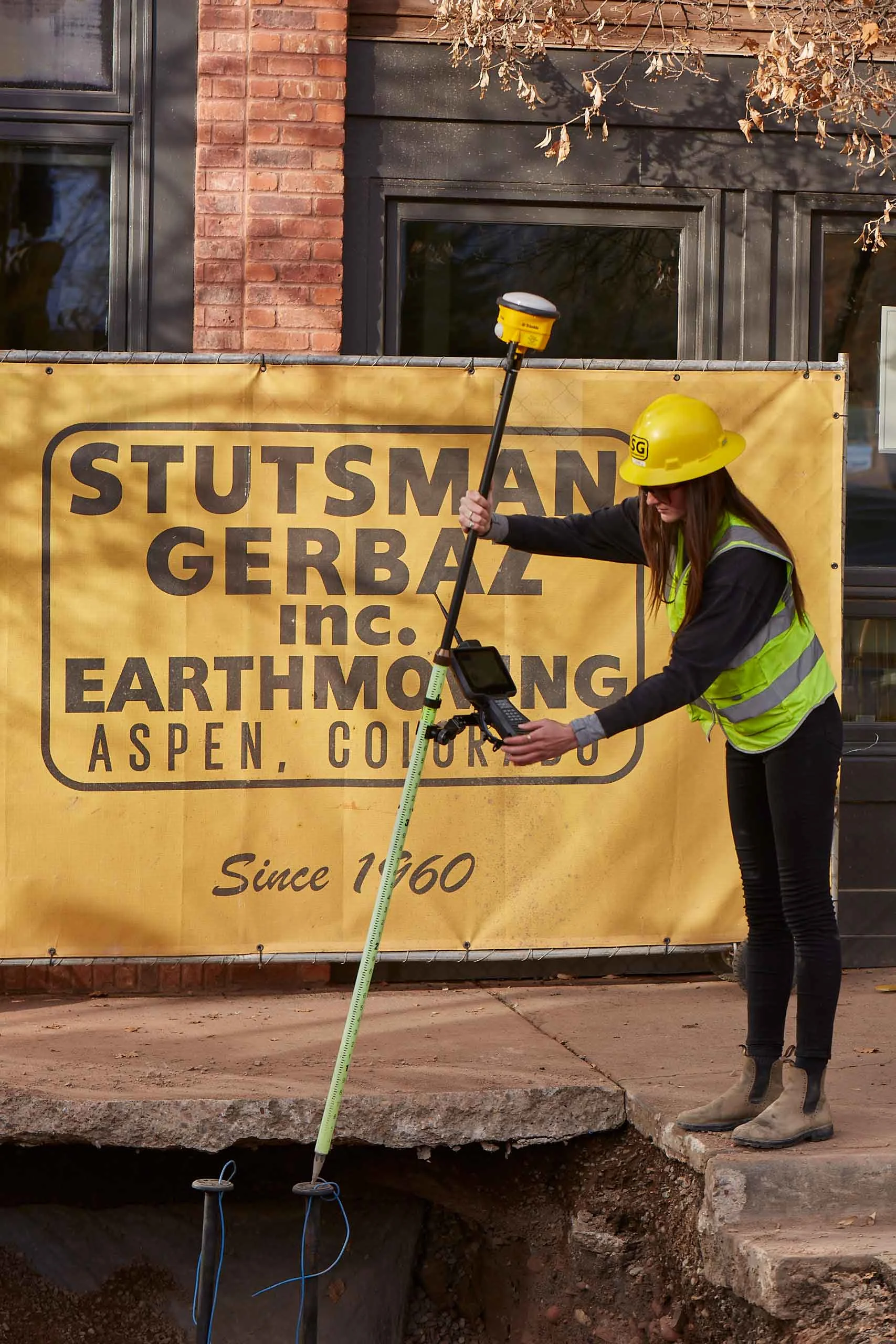 Surveyor uses GPS equipment in front of a Stutsman Gerbaz Inc. banner.