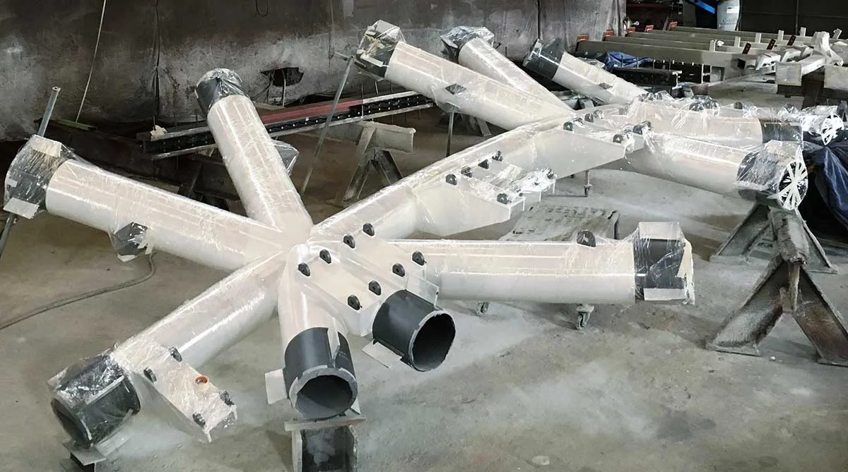 A star-shaped assembly of white pipes, some wrapped in plastic, rests on a shop floor.